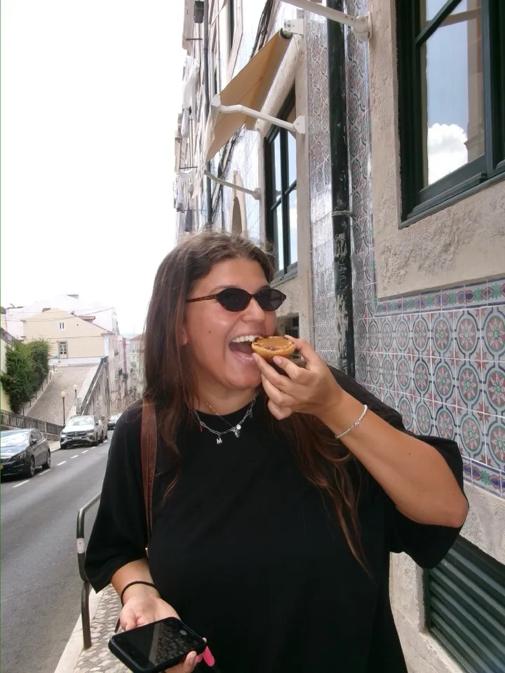Martina biting into a pastel de nata in a tiled street